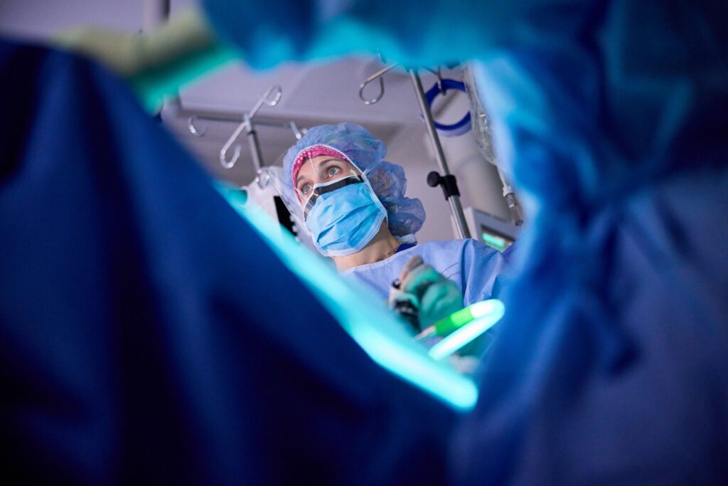 Andrea Hagemann, MD holds medical instruments while wearing a face mask and hair covering in a surgical room