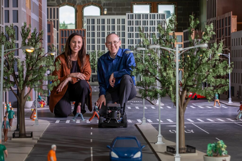 Two professors smiling within the Autonomous Vehicle City display in McKelvey Hall