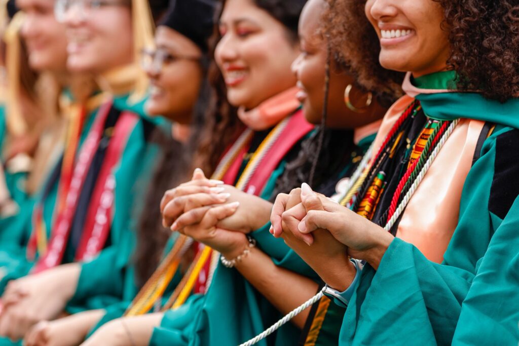 Close up of students holding hands and smiling in their graduation robes and honor cords