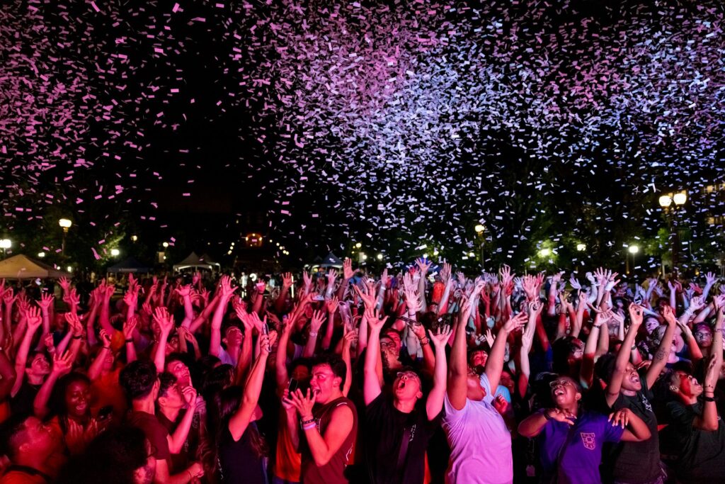 Crowd of students excitedly reach up towards confetti in the sky at nighttime